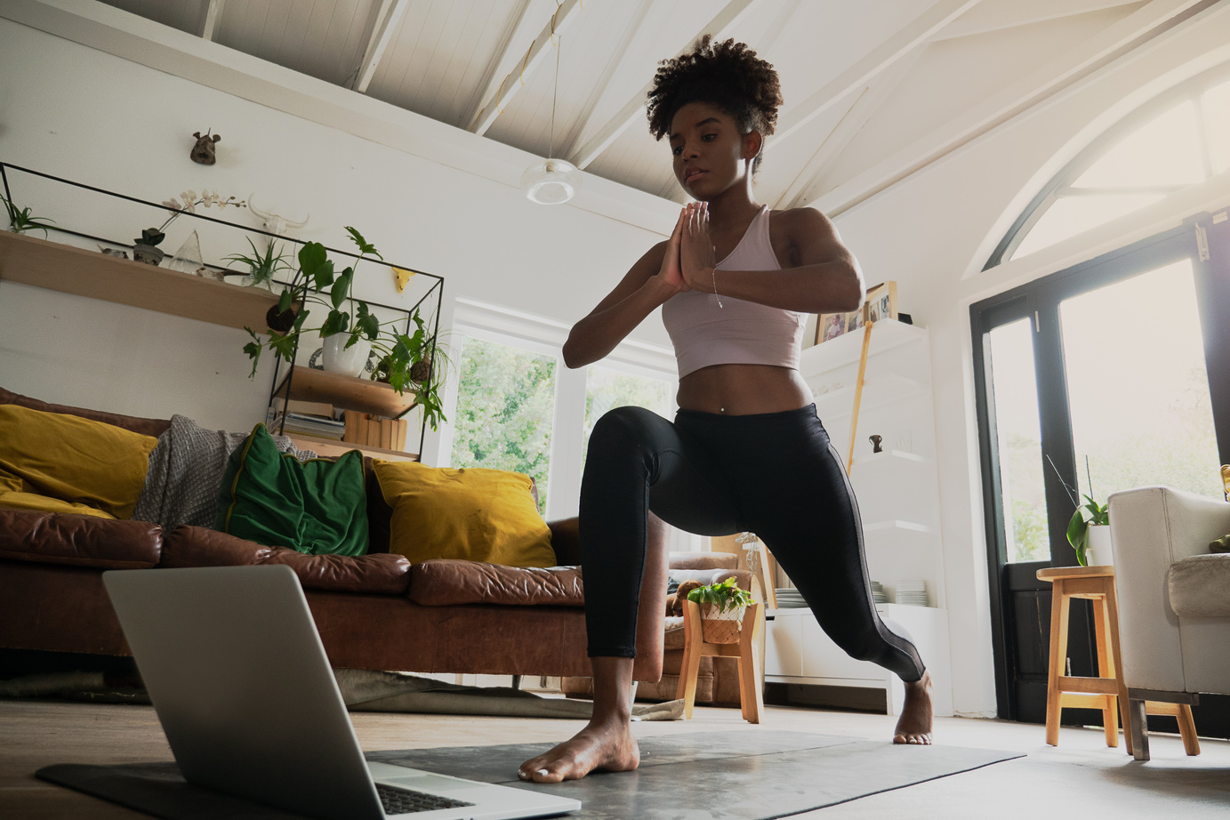 Wide angle shot of young female doing home workout or yoga from home, following an online workout on computer or online