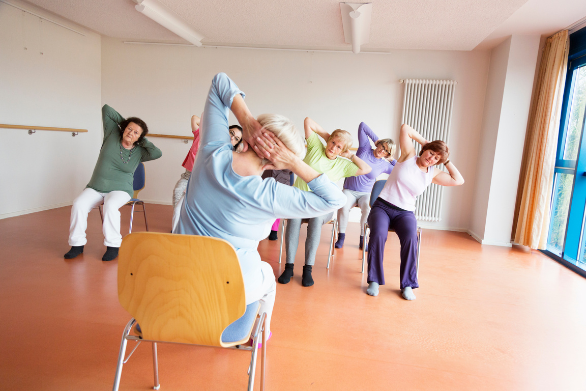 teacher and active senior women yoga class on chairs